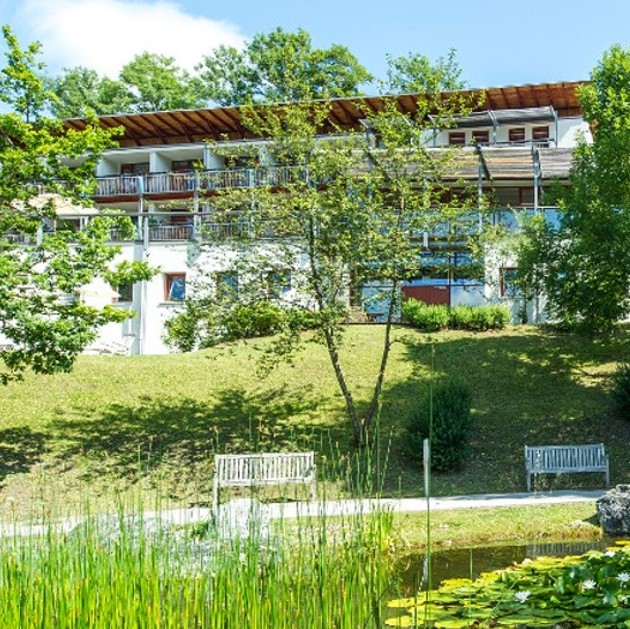 Au&szlig;enansicht des Gesundheitszentrums Goldegg. Vor dem Geb&auml;ude sind eine Wiese, B&auml;ume, ein Spazierweg, B&auml;nke und ein Teich.