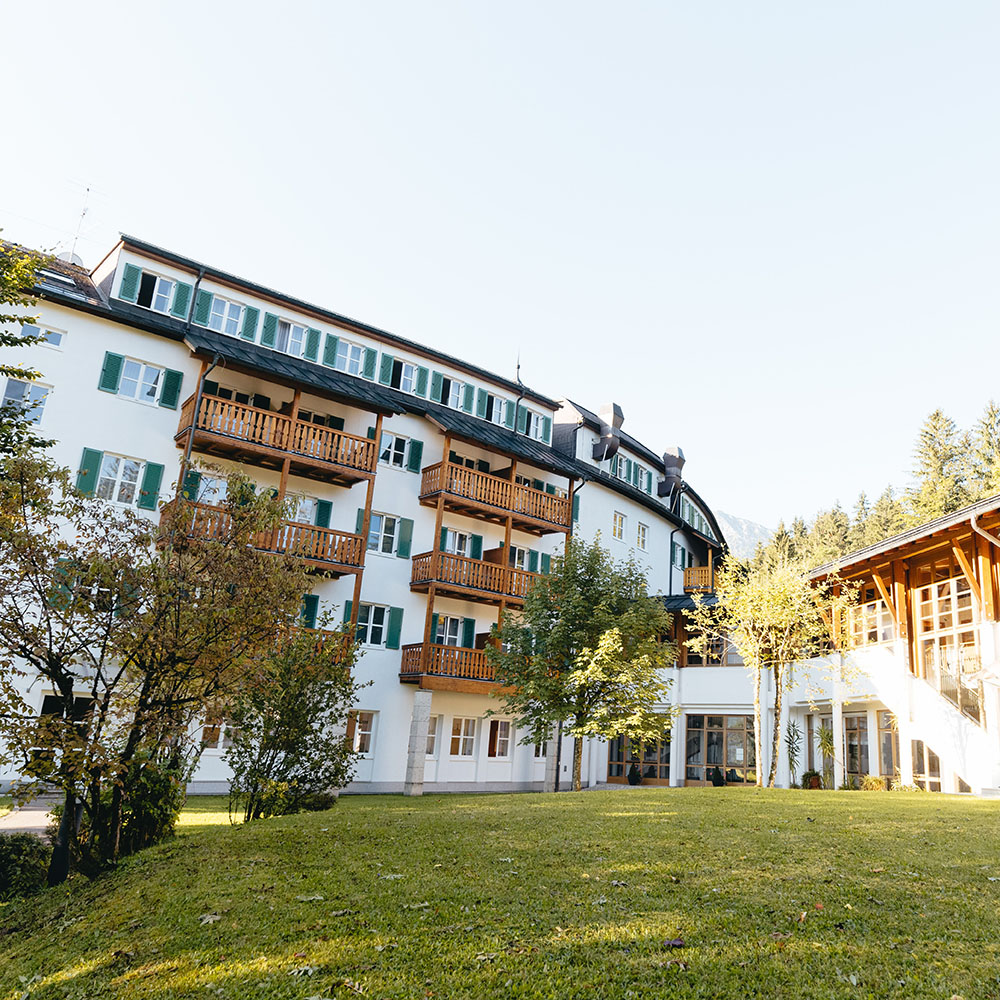 R&uuml;ckseitige Au&szlig;enansicht des Gesundheitszentrums Hanuschhof. Fenster und Holzbalkone mit Sicht auf eine Wiese mit B&auml;umen.